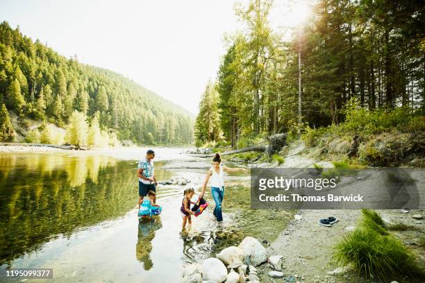 mother and father playing with daughters in river on summer afternoon - kids at river stock-fotos und bilder