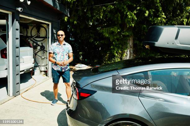 Smiling father standing behind electric car before beginning family road trip