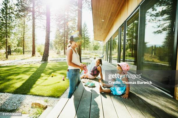 laughing mother hanging out with young daughters on front porch of vacation home on summer afternoon - luxury family stock pictures, royalty-free photos & images