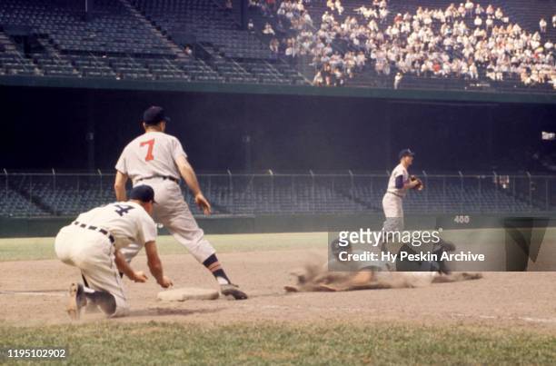 Third base coach Billy Hitchcock of the Detroit Tigers shows Eddie Yost to slide as shortstop George Strickland of the Cleveland Indians throws to...