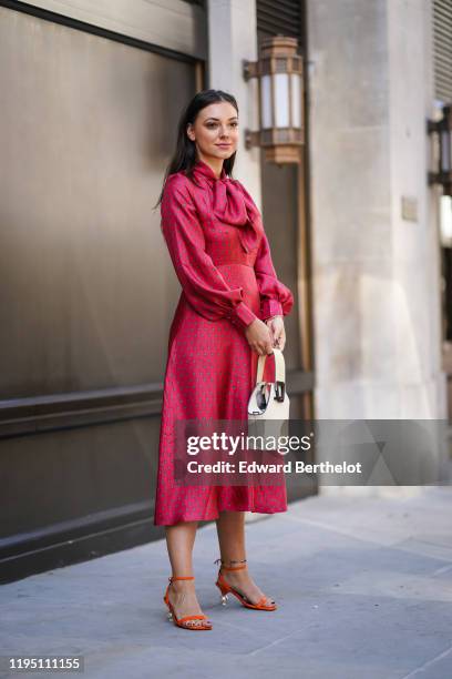 Andreea Cristea wears a red dress with printed stars, a white bag, orange shoes with silver metallic heels shaped as spheres, during London Fashion...