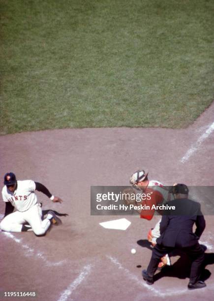 Willie Mays of the San Francisco Giants slides into home as catcher Johnny Edwards of the Cincinnati Reds can't handle the throw during an MLB game...