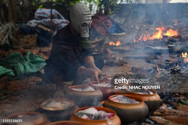 Man wears a gas mask while cooking fish in claypots over wood fire in Ha Nam province on January 21, 2020 ahead of the Lunar New Year. The braised...