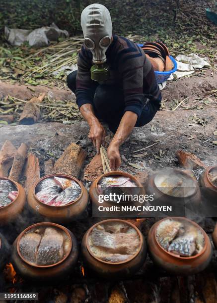 Man wears a gas mask while cooking fish in claypots over wood fire in Ha Nam province on January 21, 2020 ahead of the Lunar New Year. The braised...