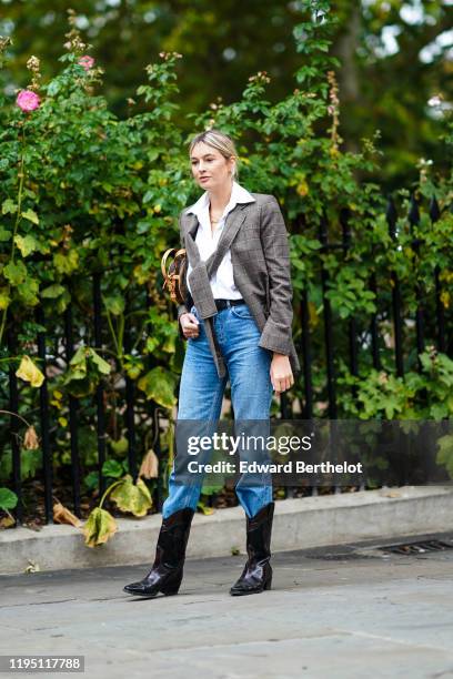 Camille Charriere wears a white shirt, a gray checked jacket, a belt, blue denim jeans, black cowboy leather boots, during London Fashion Week...