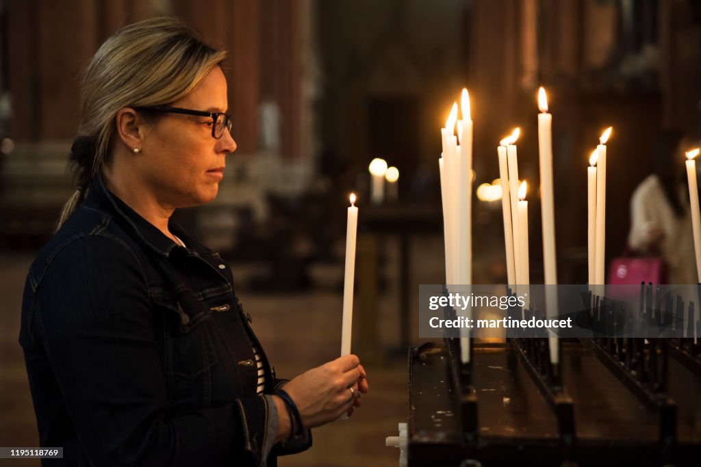 Mature woman lighting candles in church.