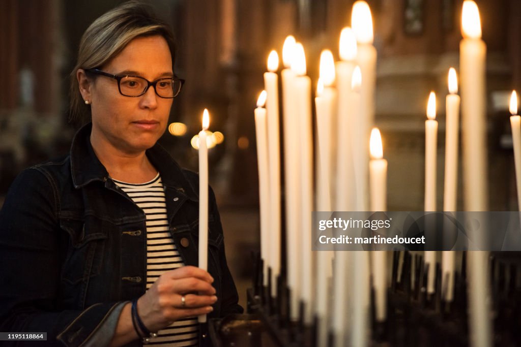 Mature woman lighting candles in church.