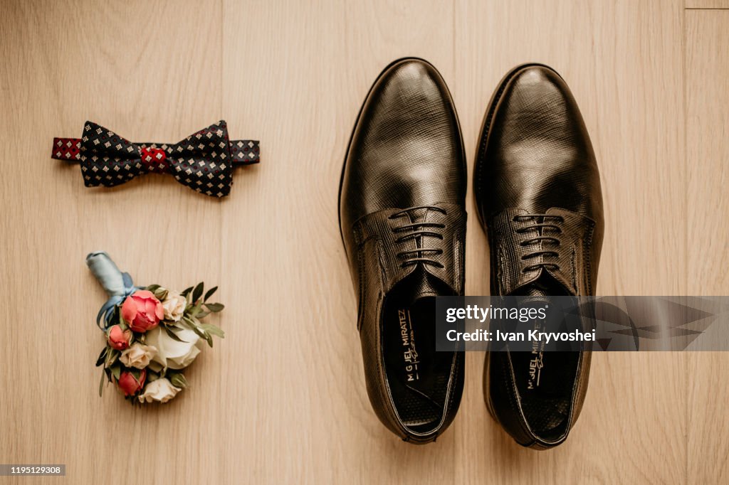 Close up of modern groom accessories. Black bowtie, leather shoes and flower boutonniere on rustic background. Set for formal style of wearing isolated on white background