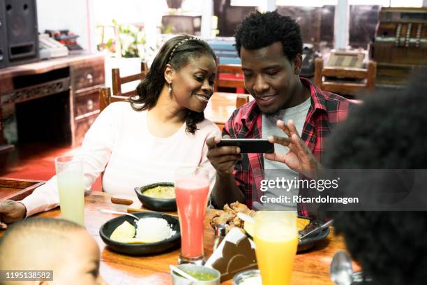 afro family taking a picture of bandeja paisa's plate, a typical dish of the plain in colombia - bandeja stock pictures, royalty-free photos & images