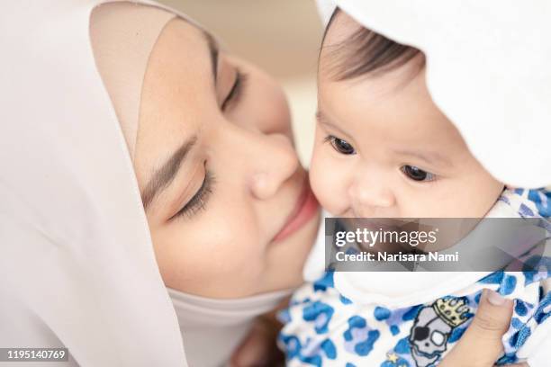 asian muslim mother woman kissing and hugging a  baby in her arms. family concept. - indonesia family stock pictures, royalty-free photos & images