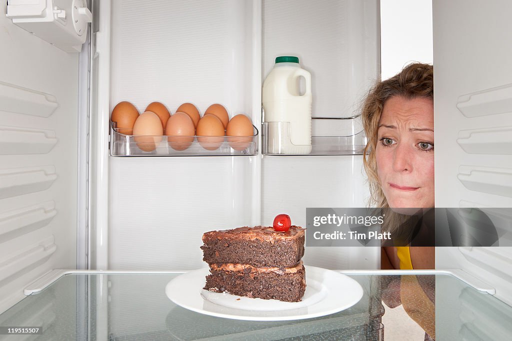 Woman looks at cake in a fridge.