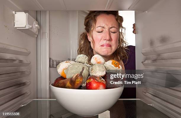 woman finds bowl of rotting fruit in the fridge. - rotting stockfoto's en -beelden