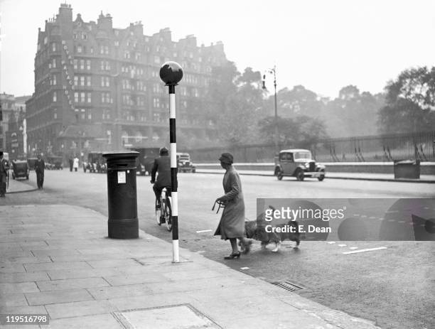 Woman crosses a road near one of the newly-introduced belisha beacons, Kensington, London, 18th September 1934. The crossing is also marked by metal...