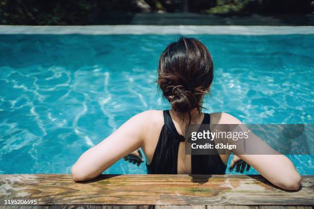 young asian woman resting on the edge of the swimming pool relaxing and enjoying the sun while on summer vacation - arm sun beach stock-fotos und bilder