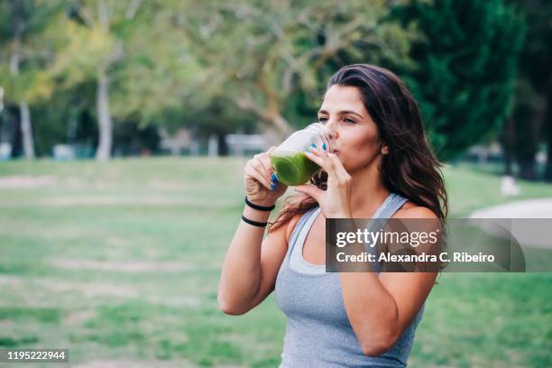 fit female personal trainer drinking green smoothie in park - frasco para conservas fotografías e imágenes de stock