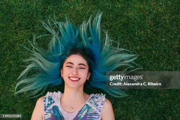 overhead portrait carefree young woman with blue hair laying in grass - alexandra summers stockfoto's en -beelden