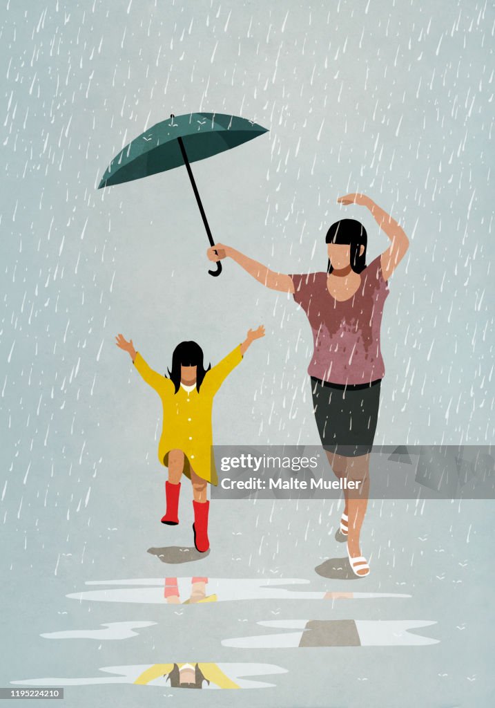 Carefree mother and daughter dancing in rain
