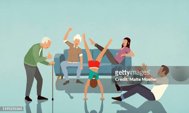 happy multi-generation family cheering for girl doing handstand in living room - family stock illustrations