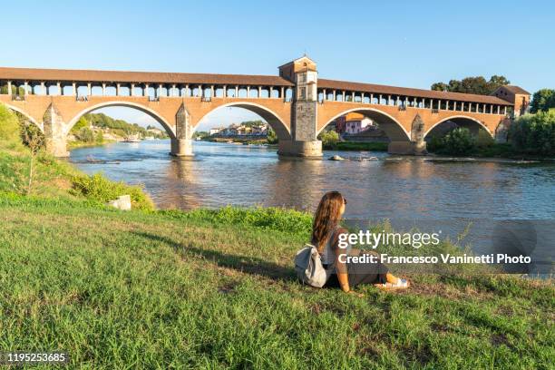 woman gazing at the old bridge and ticino river, pavia, italy. - pavia italy stock pictures, royalty-free photos & images