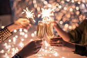 Hands of couple with flutes of champagne and their friends with bengal lights