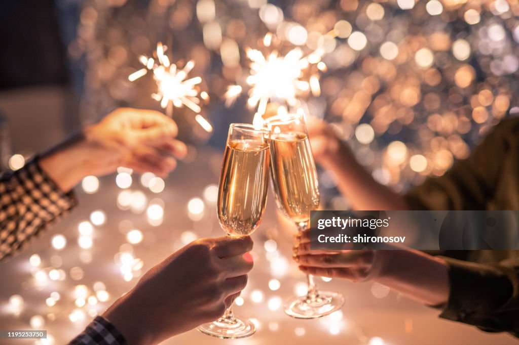 Hands of couple with flutes of champagne and their friends with bengal lights