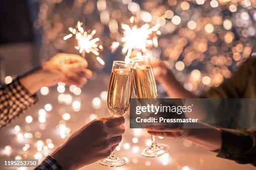 Hands of couple with flutes of champagne and their friends with bengal lights Hands of couple with flutes of champagne and their friends with bengal lights