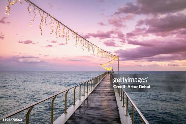 pier with christmas lights over the sea with stunning sunset sky. - noel sapin stock-fotos und bilder