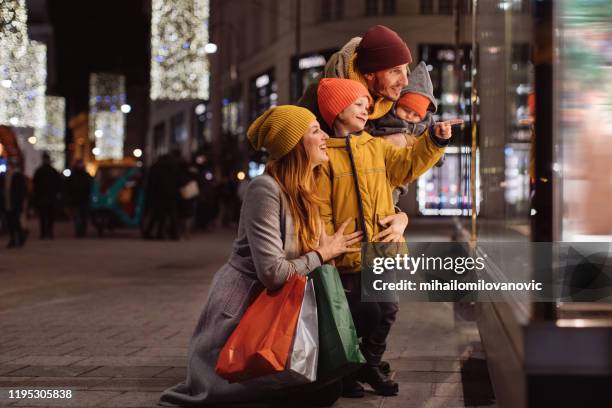 familie met twee kinderen in de voorkant van het winkel venster - etalages kijken stockfoto's en -beelden