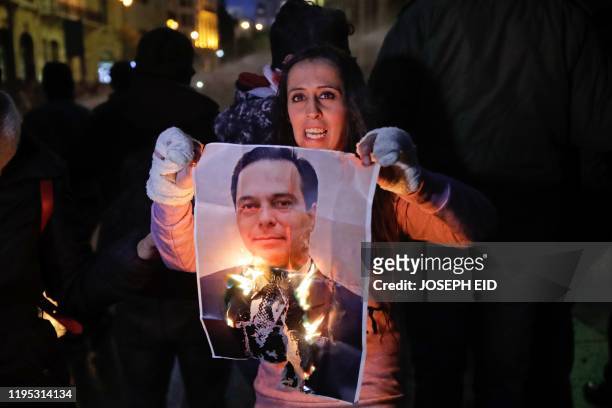 Lebanese anti-government protester burns a picture of new prime minister Hassan Diab during a protest near the parliament headquarters in the central...
