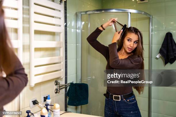 beautiful woman straightening a hair in front of the mirror - flat iron stock pictures, royalty-free photos & images