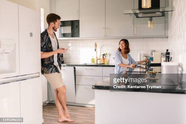smiling woman making coffee while looking at man using phone in kitchen - talk phone flat imagens e fotografias de stock