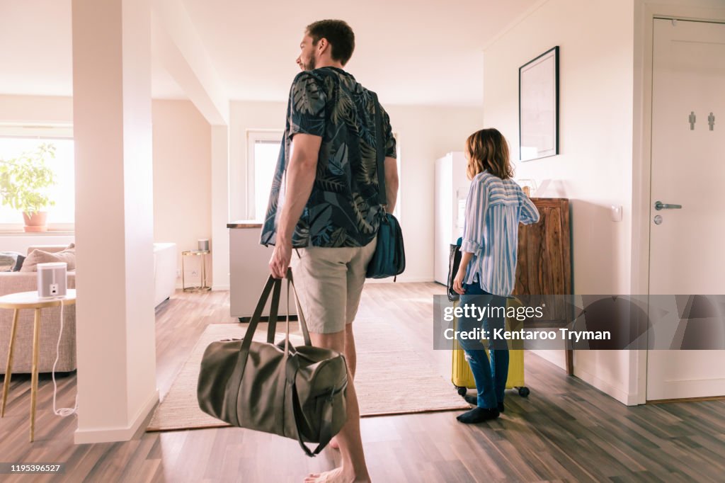 Couple walking with luggage in apartment during staycation