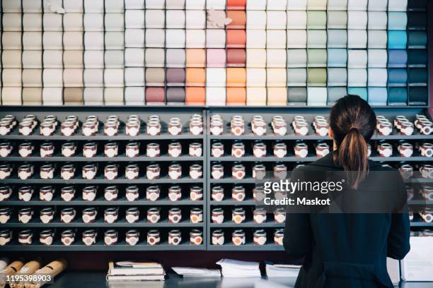 rear view of woman choosing wallpapers and paints displayed for sale in store - tool rack ストックフォトと画像