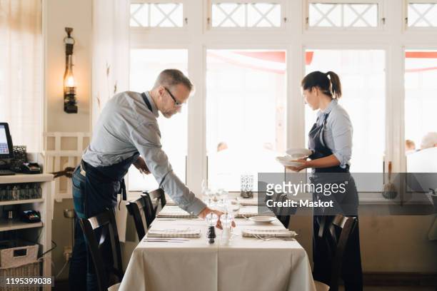 male and female coworkers arranging table in restaurant - arrangiare foto e immagini stock