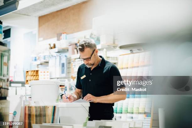salesman in uniform writing on document in hardware store - bouwmarkt stockfoto's en -beelden