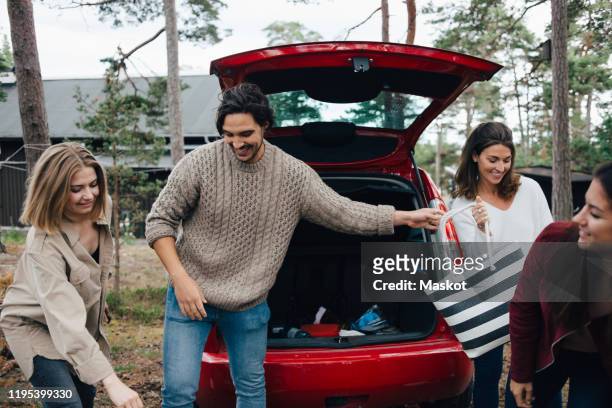 male and female friends unloading luggage from car in back yard - offloading stock-fotos und bilder