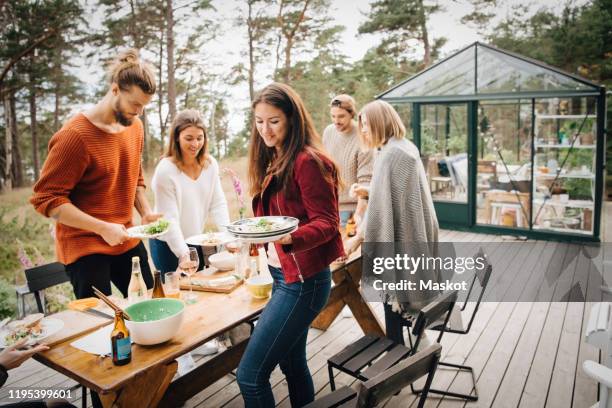 male and female friends carrying leftover plates after dinner at patio - friends clean stock pictures, royalty-free photos & images