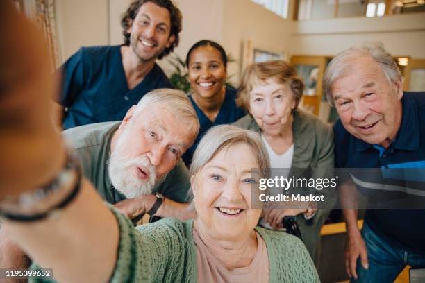 retired elderly woman taking selfie with friends and caregivers at retirement home - retirement community stock pictures, royalty-free photos & images