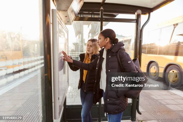 friends reading map while standing at bus stop in city - winter coat stock pictures, royalty-free photos & images