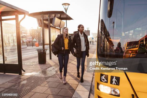 full length of friends walking on footpath towards bus in city - bus lane stockfoto's en -beelden