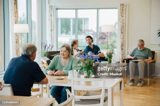 retired senior men and women sitting with male nurse at elderly nursing home - retirement village stock pictures, royalty-free photos & images