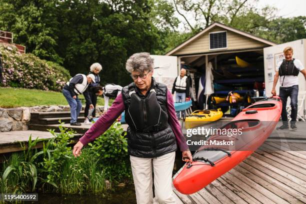 senior woman and man carrying kayak on jetty during kayaking course - carrying kayak stock pictures, royalty-free photos & images