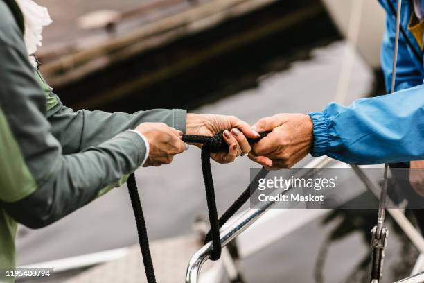cropped hands of female instructor and senior man tying rope on yacht's railing - hands tied up stock pictures, royalty-free photos & images