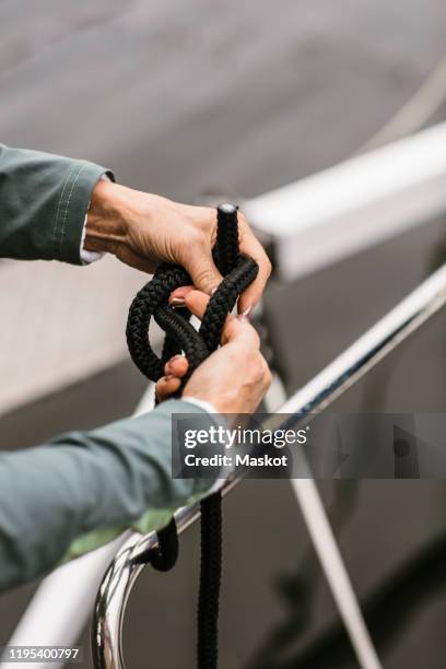 cropped hands of senior female instructor tying rope on yacht's railing - tying stock pictures, royalty-free photos & images