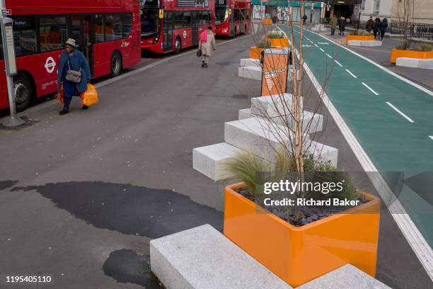 Local lady carries her orange supermarket bag towards her bus, alongsode a new cycling path, a regenerated landscape created outside Croydon College...
