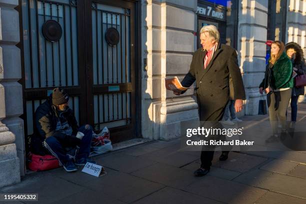 Passers-by ignore a homeless man begging with a sign saying 'I'm hungry', on the pavement in Piccadilly, on 20th January 2020, in London, England.