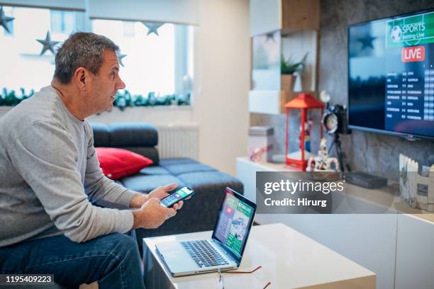 senior man watches soccer game and bets in his living room - tv addict stock pictures, royalty-free photos & images