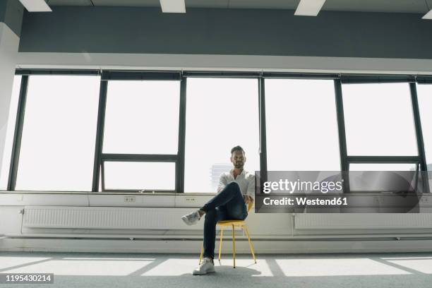 mature businessman sitting on yellow chair in empty office - man office chair stock pictures, royalty-free photos & images