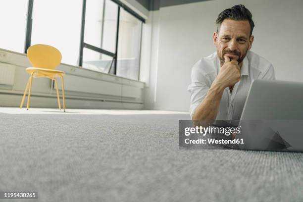 portrait of mature businessman lying on the floor in empty office using laptop - office carpet stock pictures, royalty-free photos & images