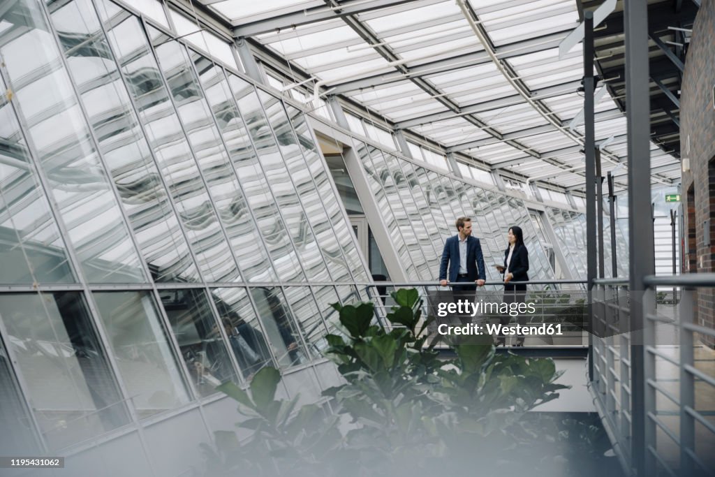 Businessman and businesswoman standing on a skywalk in modern office building